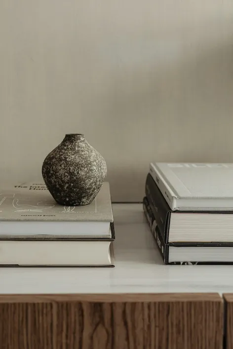 Stapel boeken met daarop een klein keramieken vaasje, in warme neutrale tinten