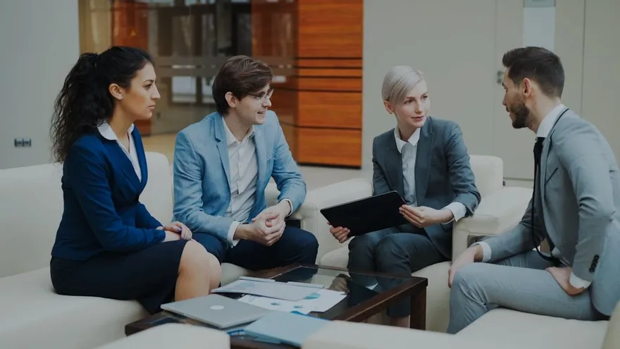 Vier professionals in gesprek tijdens een overleg, één van hen houdt een tablet vast